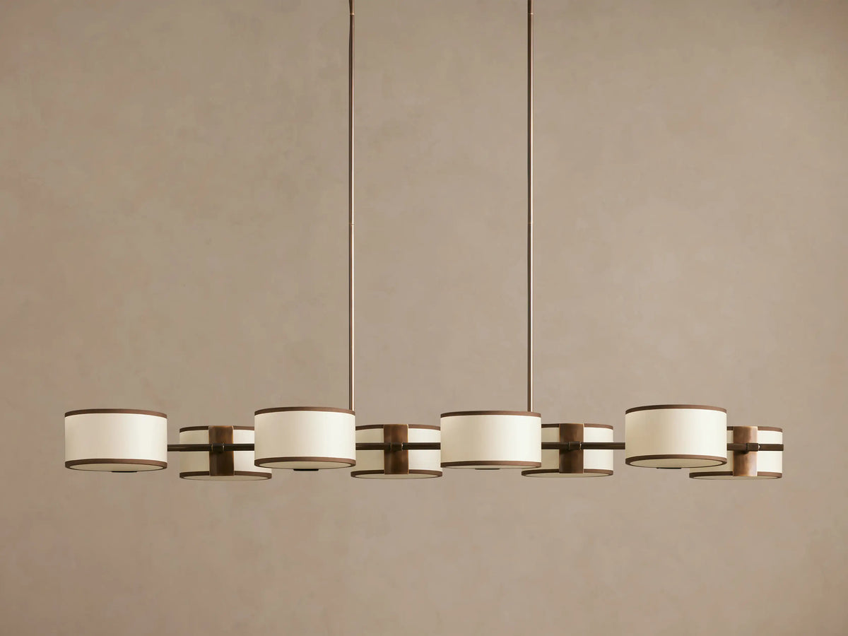 Daphne Fabric Linear Chandelier. Bronze frame, 6 white linen drum shades with black trim, hanging from ceiling.