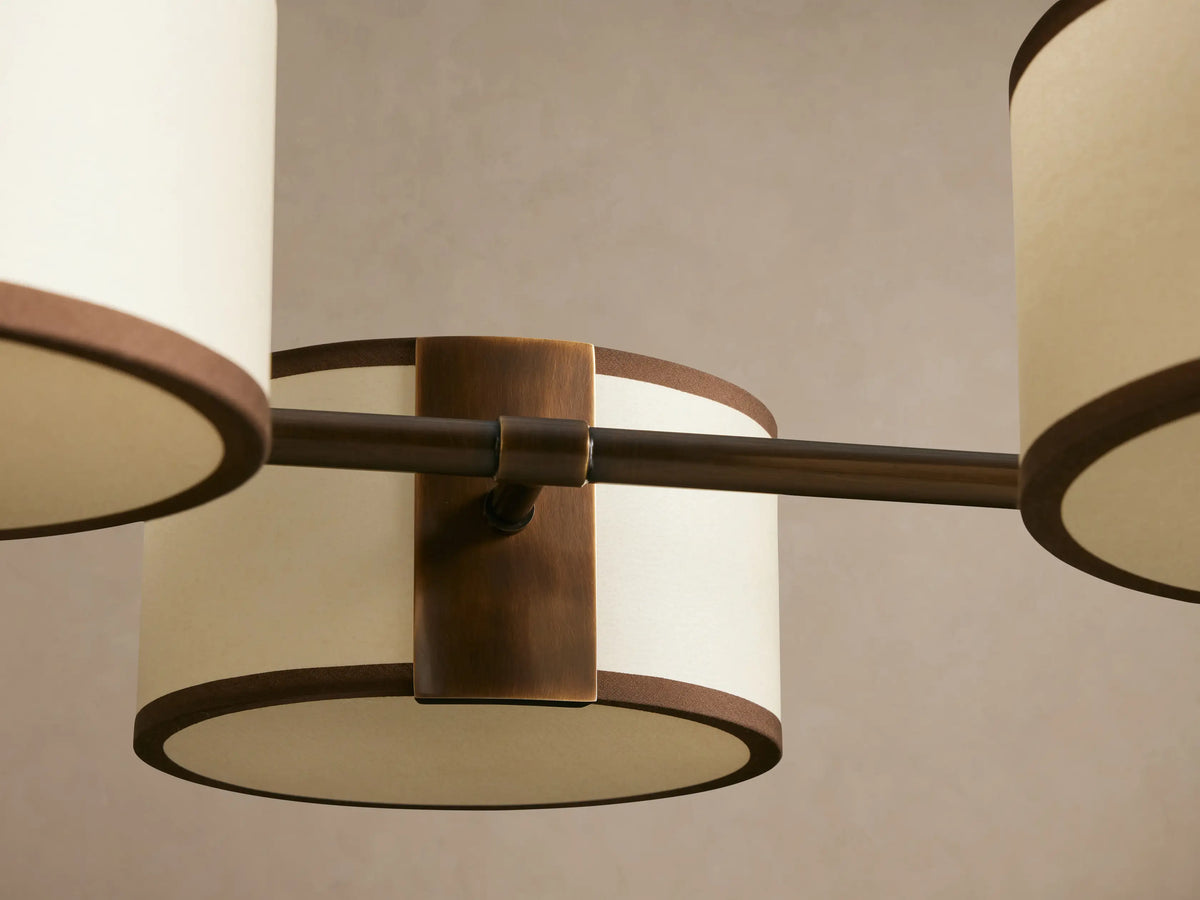 Daphne linear chandelier with 6 white linen drum shades, black trim, and dark bronze frame, suspended by two rods.