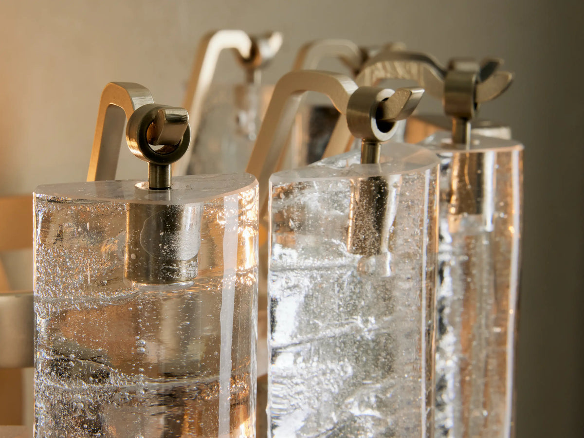 Neve Sconce close-up: textured clear & bronze cast glass rods mixed with champagne metallic elements, layered, with a warm glow.