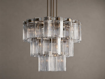 Delsie Round Chandelier, multi-tiered with clear ribbed glass rods and burnished brass frame, hanging against a brown wall.