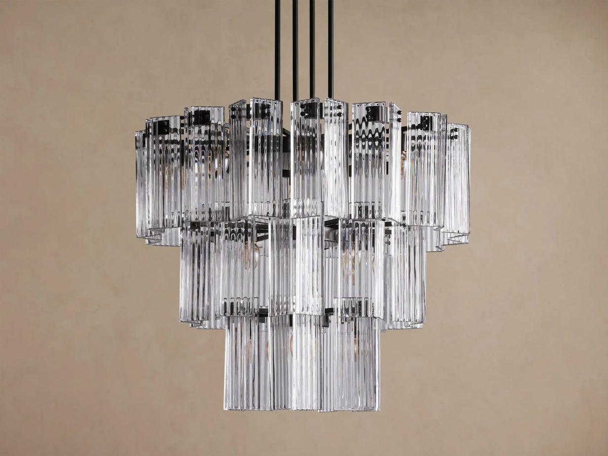 Delsie Round Chandelier, multi-tiered with clear ribbed glass rods and dark metal frame, hanging against a solid brown wall.