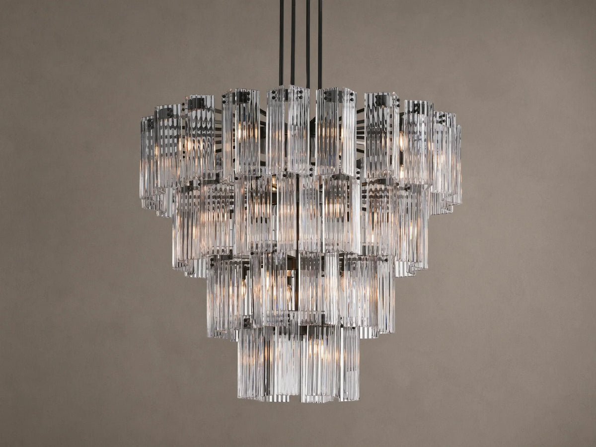 Delsie Round Chandelier with illuminated tiers of clear, fluted glass rods and a dark metal frame hanging against a taupe wall.