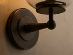 Close-up of the antique bronze Fulton Sconce with a clear glass globe and an illuminated bulb, mounted on a light wall.