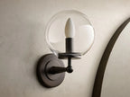 Close-up of the antique bronze Fulton Sconce with a clear glass globe, mounted on a textured wall.