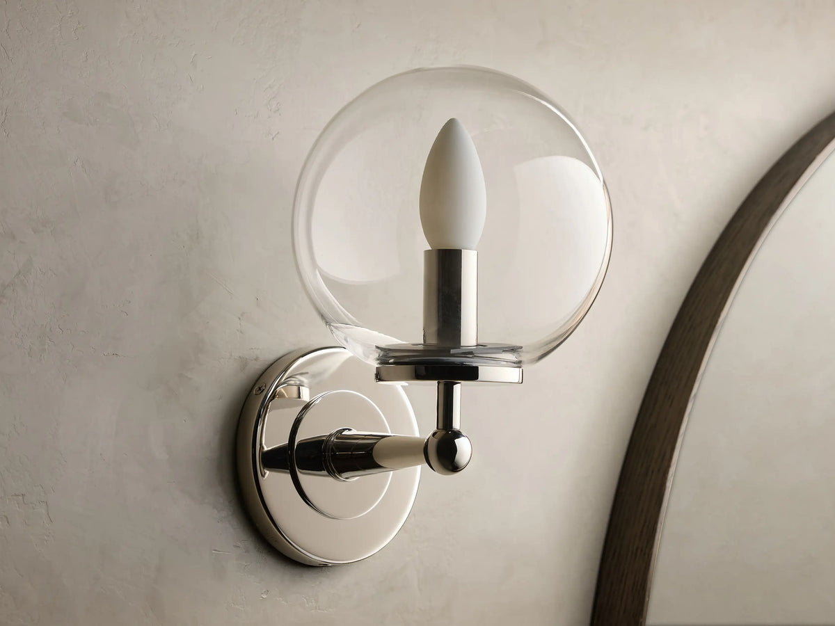 Front view of Polished Nickel Fulton Sconce with a clear glass globe and a white candle-shaped bulb on a gray wall.