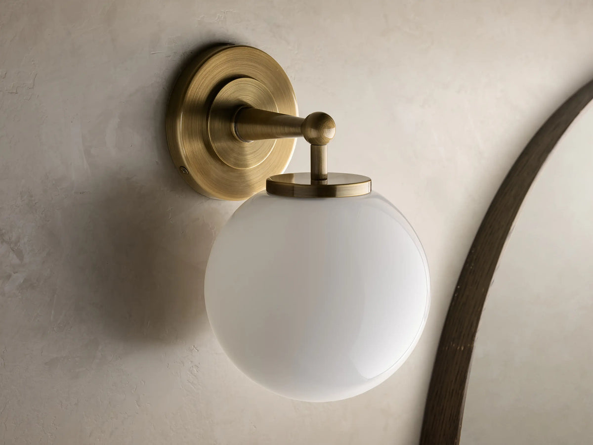 Close-up of the antique brass Fulton Sconce, featuring a glowing milk glass globe.