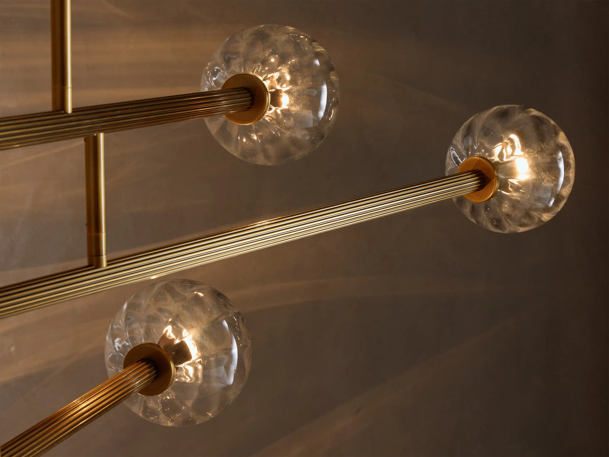 Close-up of an illuminated Brass and Glass Globe Chandelier‚Ñ¢ with clear, textured glass orbs and ribbed gold-toned arms.