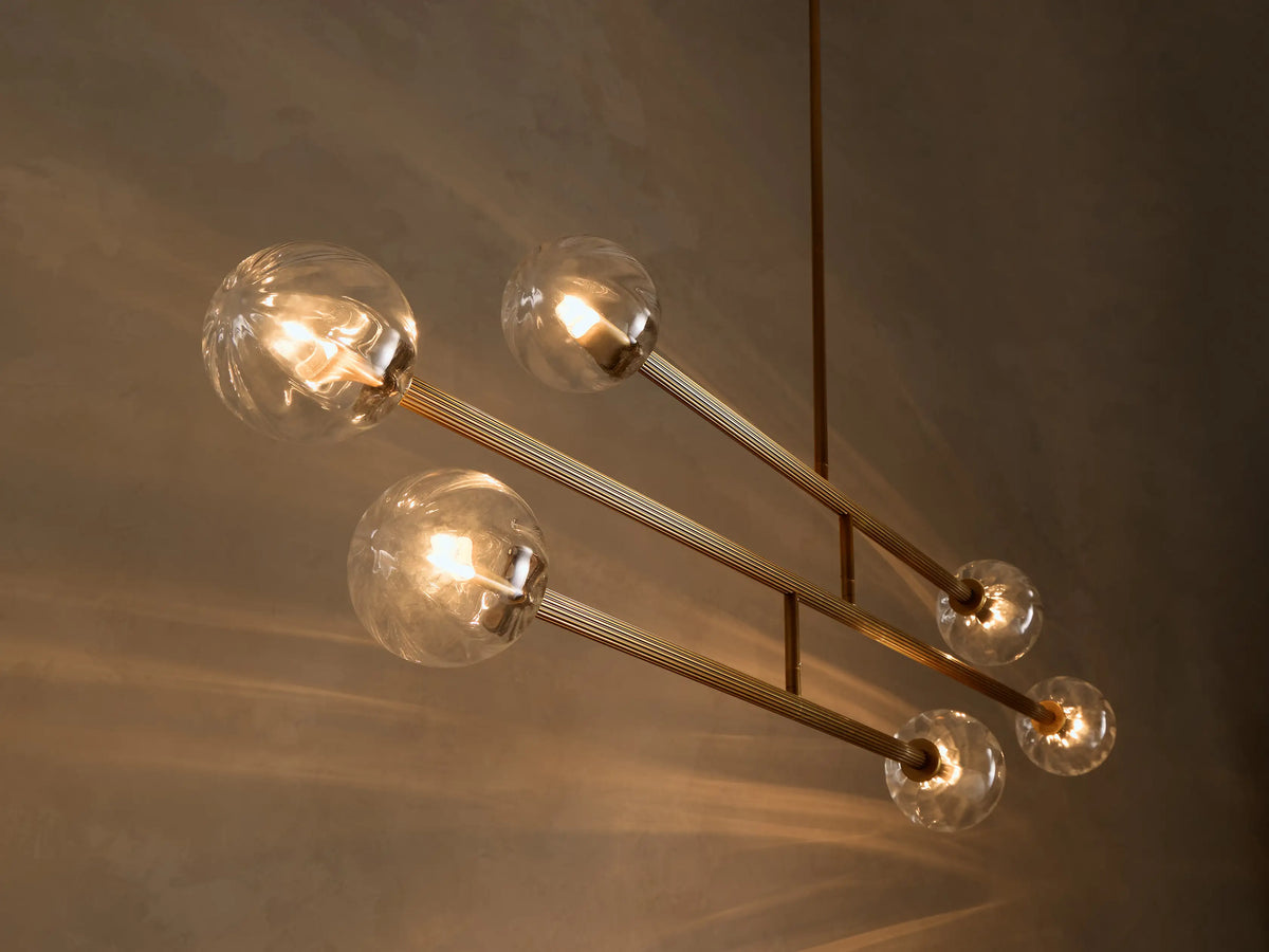 Four illuminated clear glass globe lights attached to ribbed brass-toned metal rods, angled down against a dark wall.
