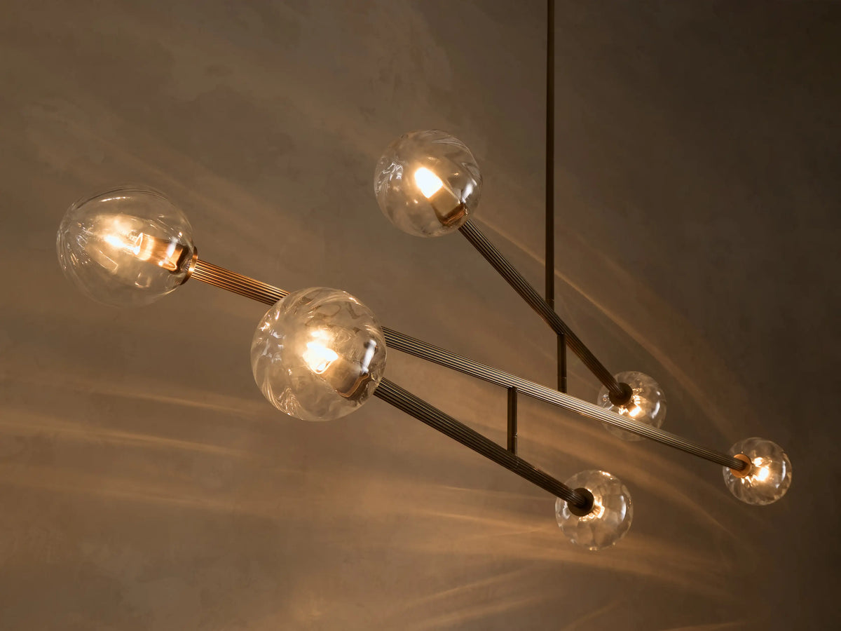 Close-up of a modern chandelier with clear glass globes, some textured, on dark metal rods, illuminating a warm glow.