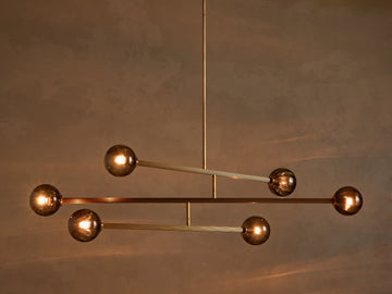 Modern chandelier with a vertical brass rod, horizontal ribbed brass arms, and six illuminated spherical smoky glass bulbs.