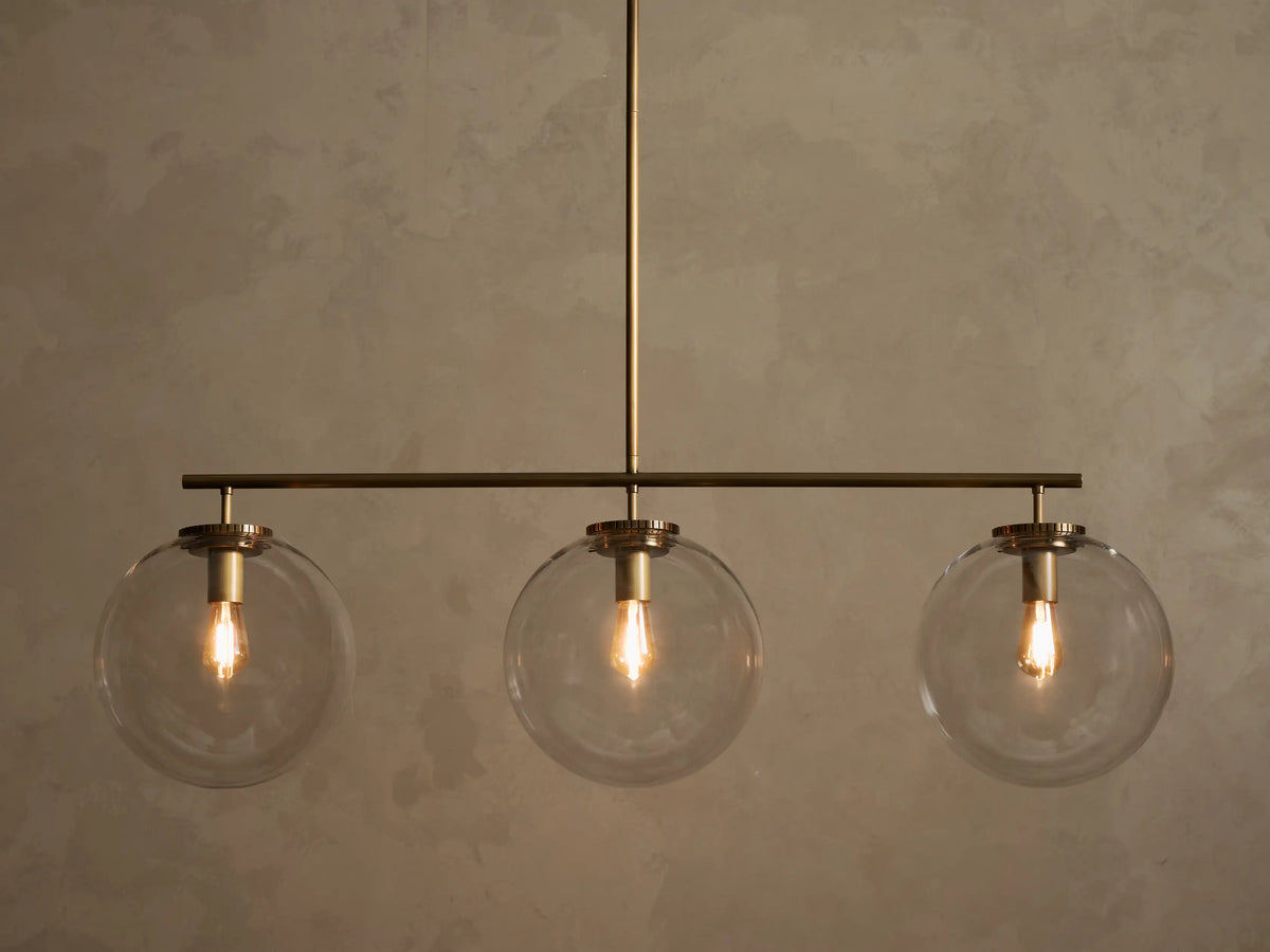 Front view of a brass chandelier with three clear glass globe shades, each containing an illuminated filament bulb.