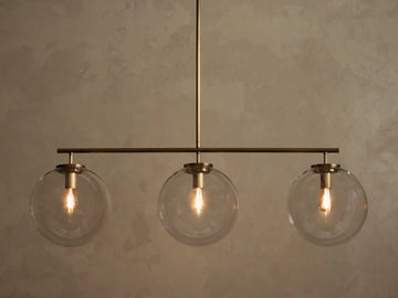 Front view of a brass chandelier with three clear glass globe shades, each containing an illuminated filament bulb.
