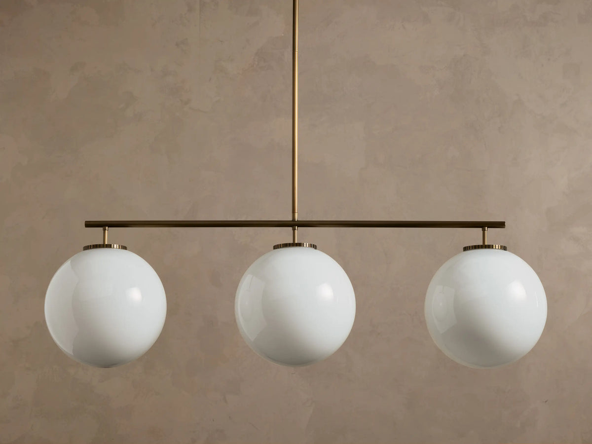 Front view of a multi-globe pendant light with three white spherical glass globes on a bronze bar.