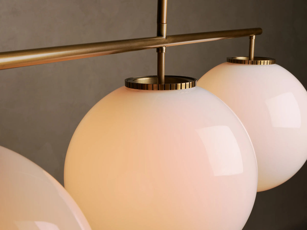 Front view of a modern brass-tone pendant light with three white globe shades on a horizontal bar, suspended from above.