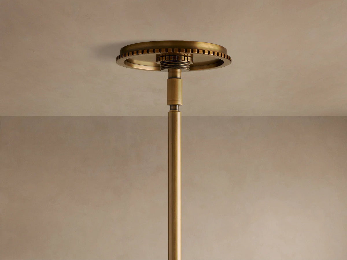 Three-light brass and clear glass pendant fixture with exposed filament bulbs glowing, suspended from a rod.
