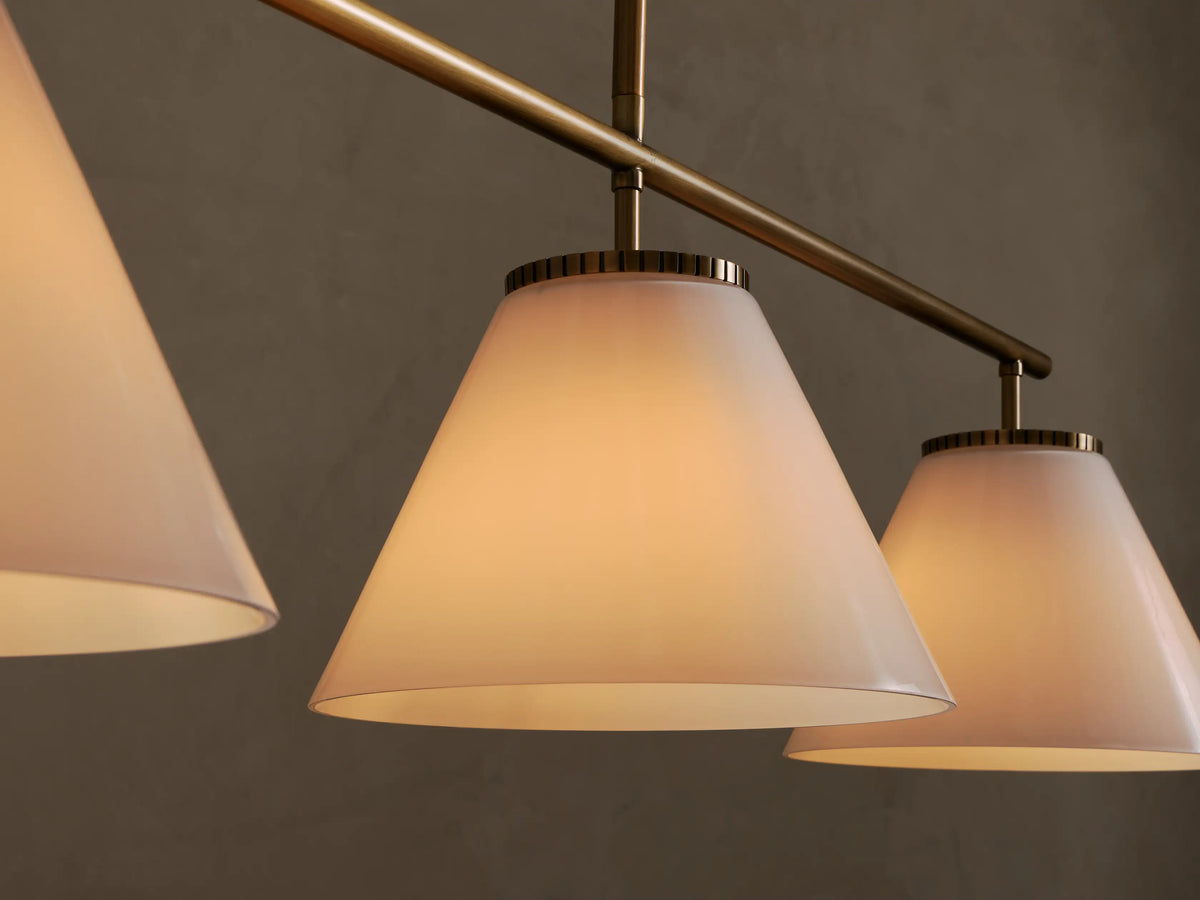 Three-light linear chandelier with white conical shades and brass-finished suspension rod and hardware.