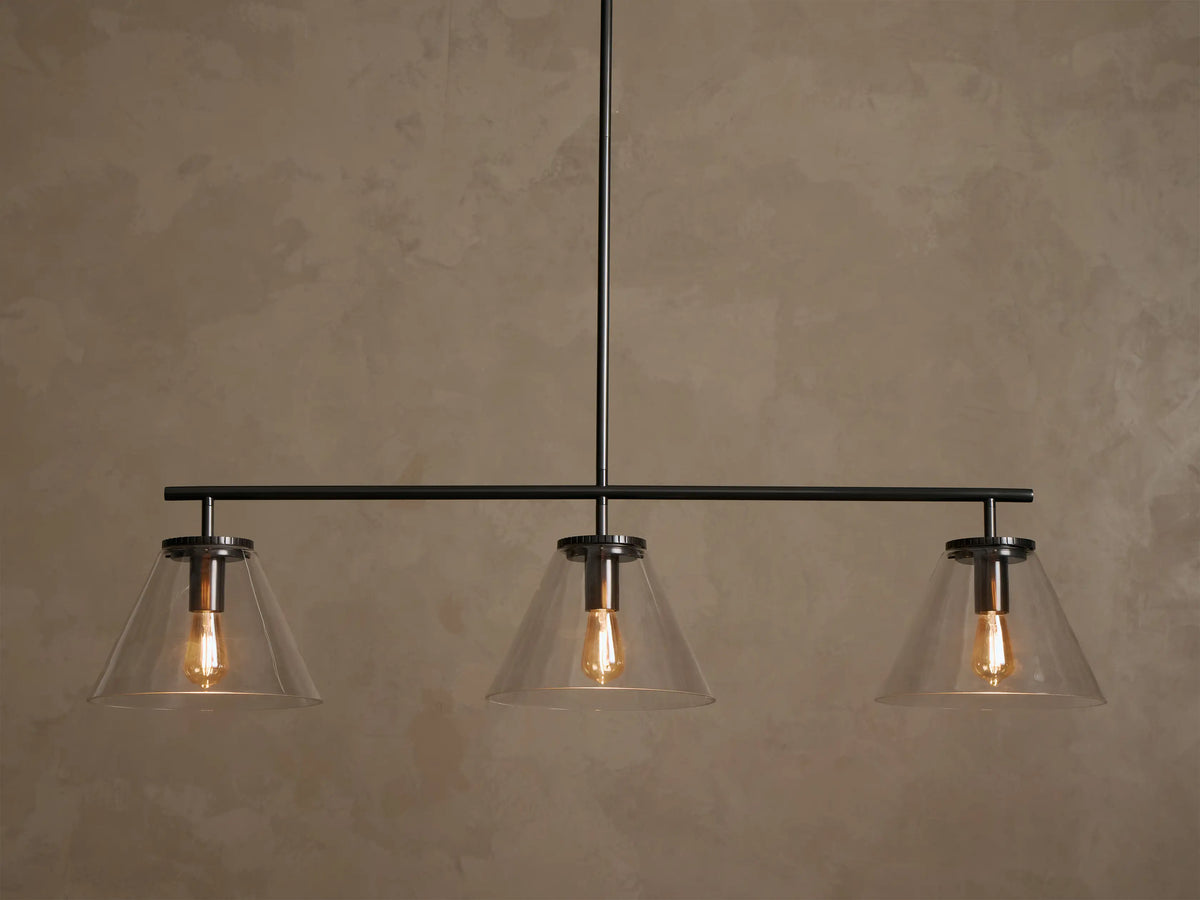 Front view of a black linear pendant light fixture with three clear conical glass shades and exposed warm Edison bulbs.