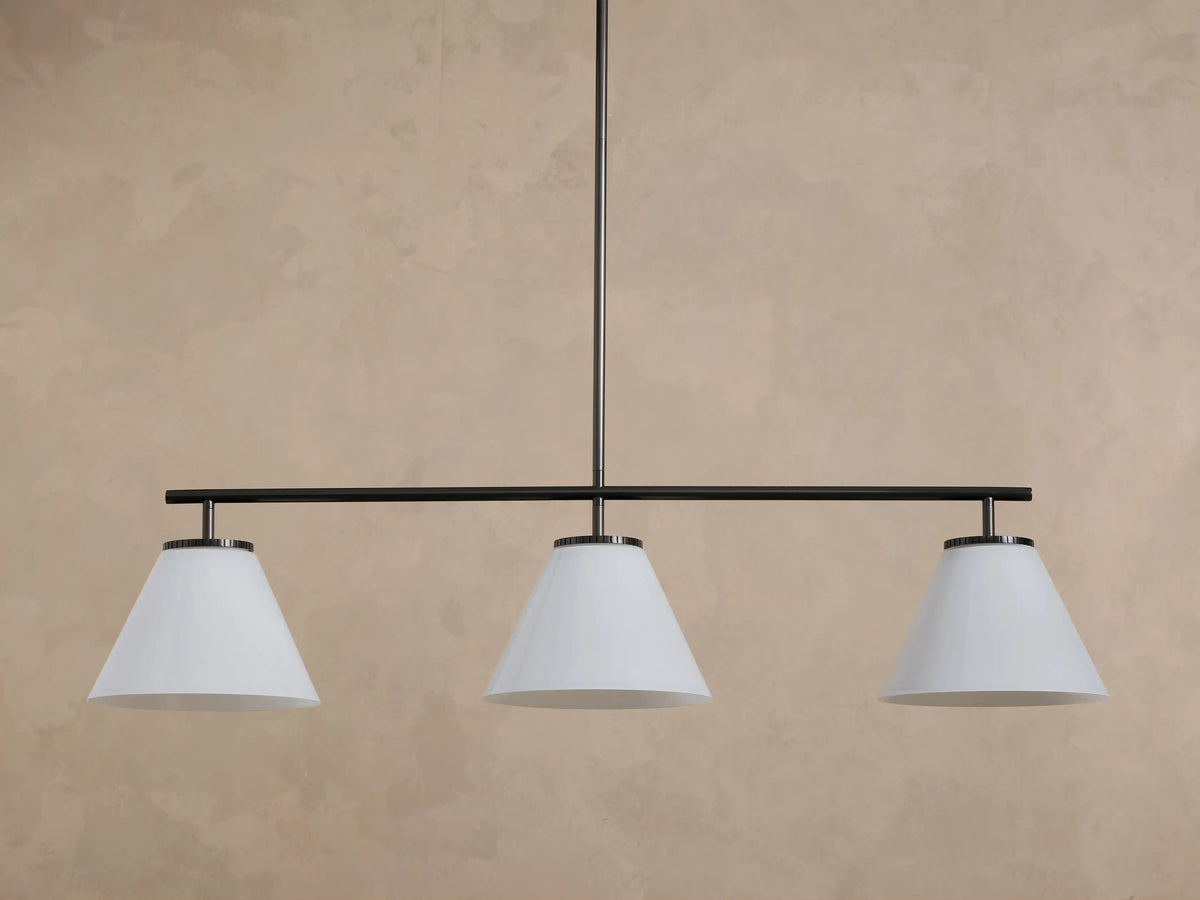 Front view of a three-light linear pendant chandelier with white conical shades and a dark bronze finish.