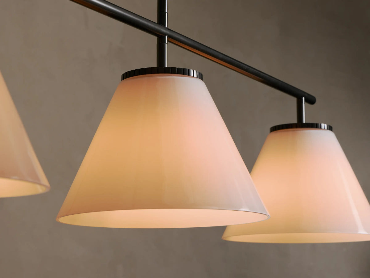 Close-up of three illuminated conical opal glass shades on a dark metal light fixture.
