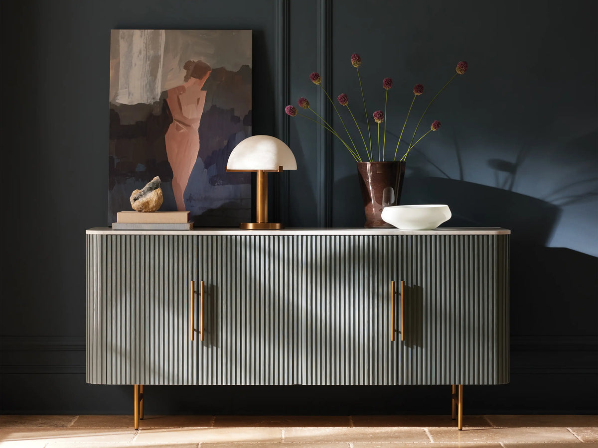 Emerie Table Lamp with alabaster stone shade and brass base on a wooden table, softly lit. Black fabric cord visible.