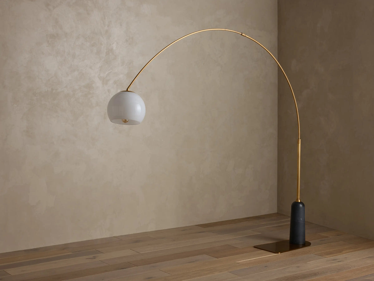 Christie Floor Lamp, arc-shaped with a brass-finished steel frame, dark natural stone base, and white milk glass shade.
