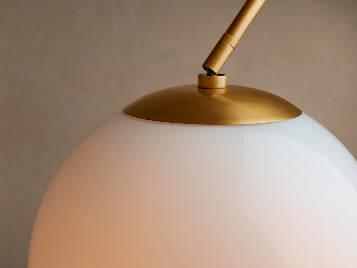 Close-up of Christie Floor Lamp's glowing, dome milk glass shade connected to its polished brass-finished arm.