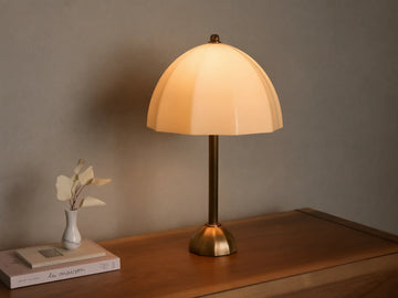 Front view of a cream ribbed glass table lamp with a brass stem and base, casting a warm glow on a wooden surface.