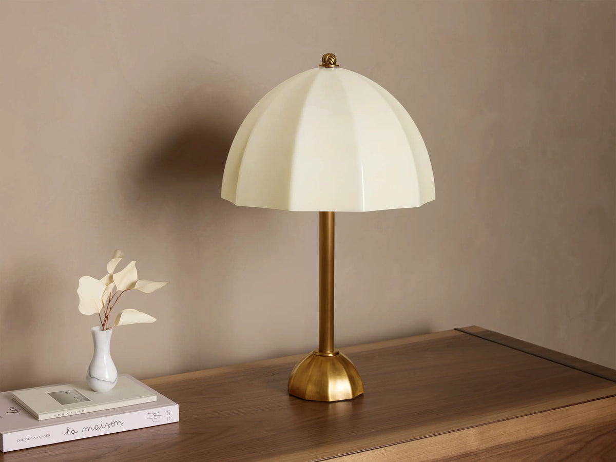 Front view of a cream ribbed glass table lamp with a brass stem and base, casting a warm glow on a wooden surface.