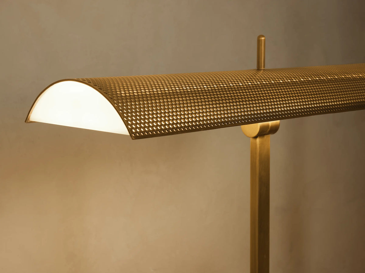 Abel Metal Floor Lamp in golden brass, with a rectangular base, slender stand, and curved perforated shade, on wood floor.