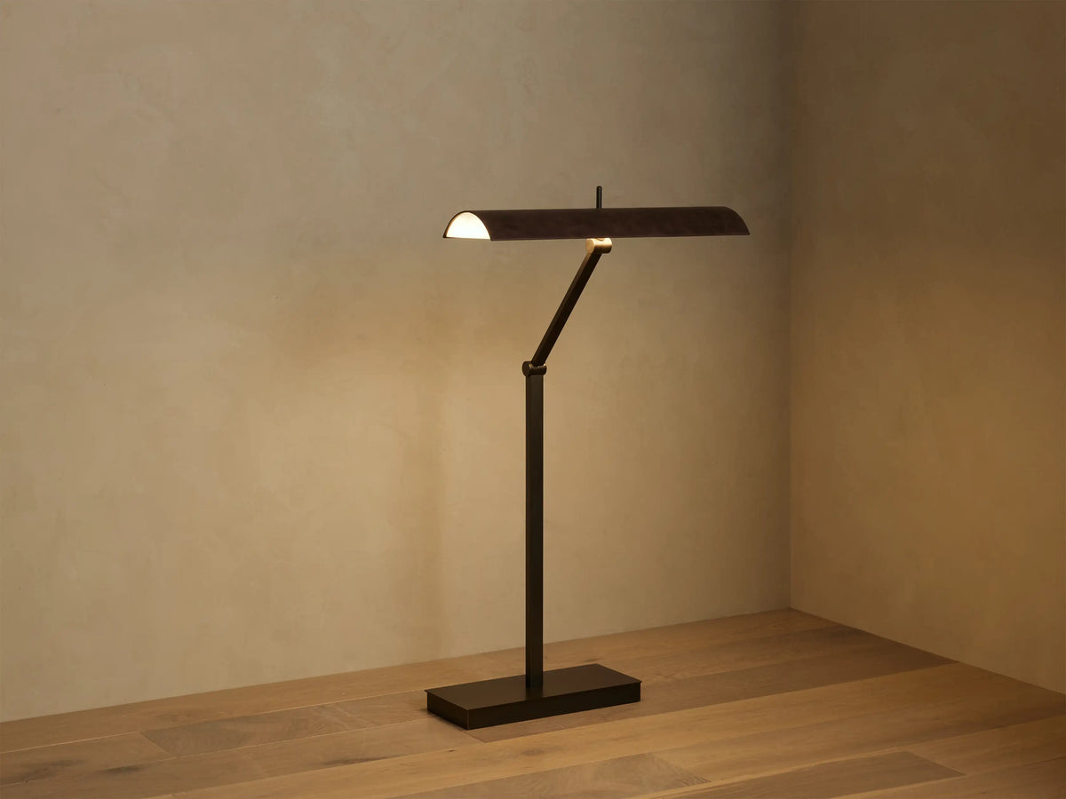 Close-up of Abel Leather Floor Lamp: horizontal dark brown leather shade glowing with warm LED light, bronze arm below.
