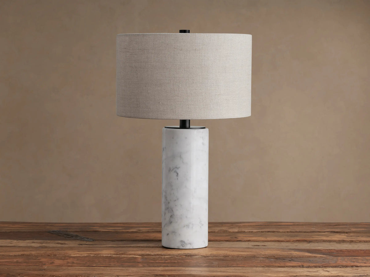 Brixton Table Lamp with cylindrical white marble base, black metal stem, and light beige fabric drum shade on a wooden table.