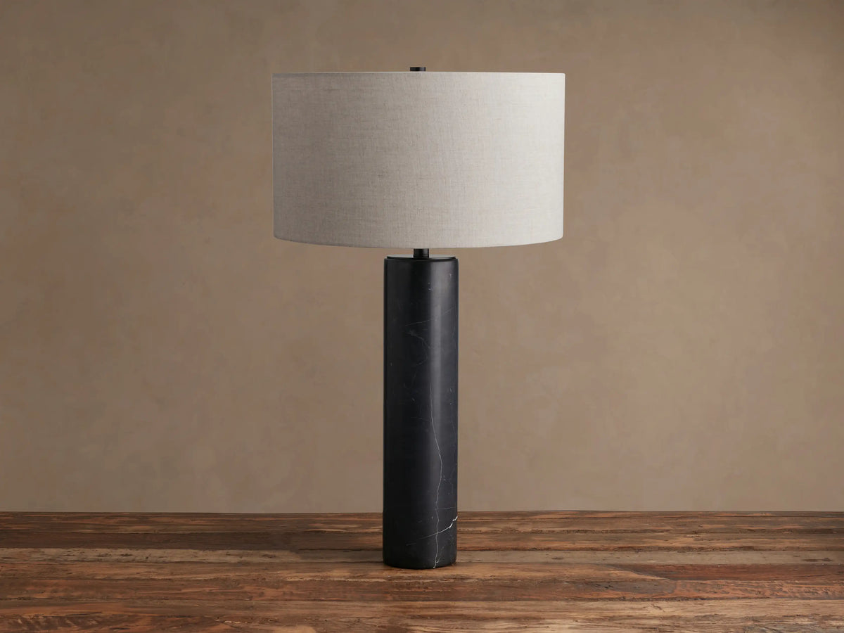 Brixton Table Lamp with a black marble cylindrical base and a light gray fabric drum shade, standing on a wooden surface.