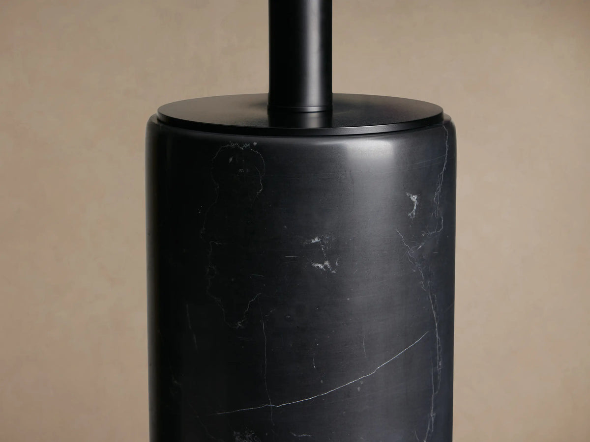 Brixton Table Lamp with a dark grey marble cylindrical base featuring white veining, topped by a light beige fabric shade, on a wooden table.