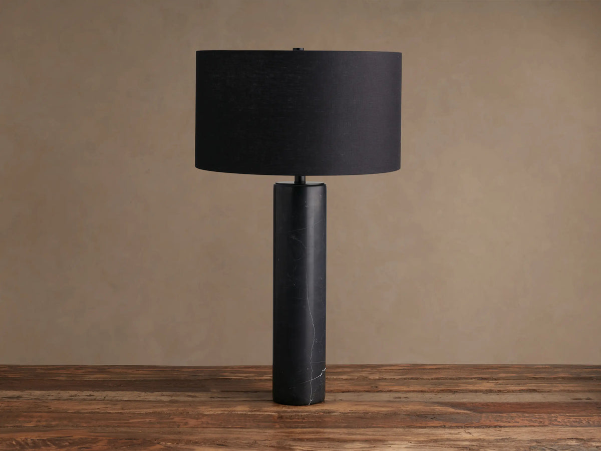 Brixton Table Lamp with a black marble column, brass accent, and dark fabric drum shade on a rustic wood table.