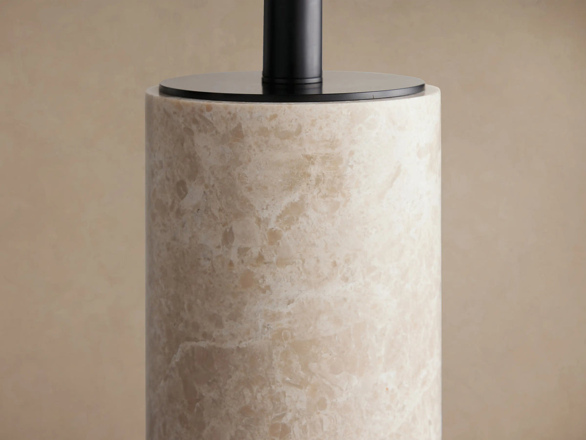 Brixton Table Lamp with a natural light marble cylindrical base and a textured beige fabric drum shade, on wood.
