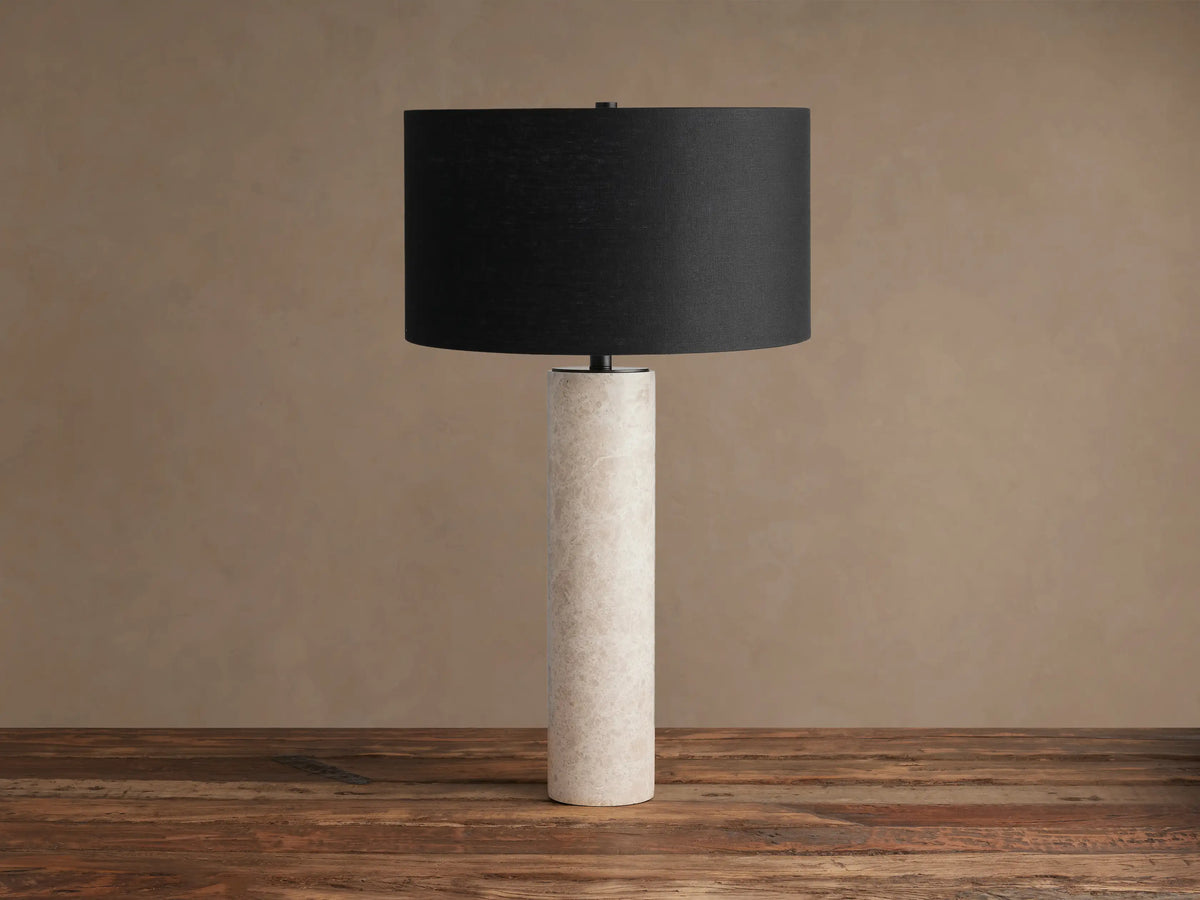 Brixton Table Lamp with a black cylindrical shade and a tall, cream-colored marble base, standing on a wooden table.