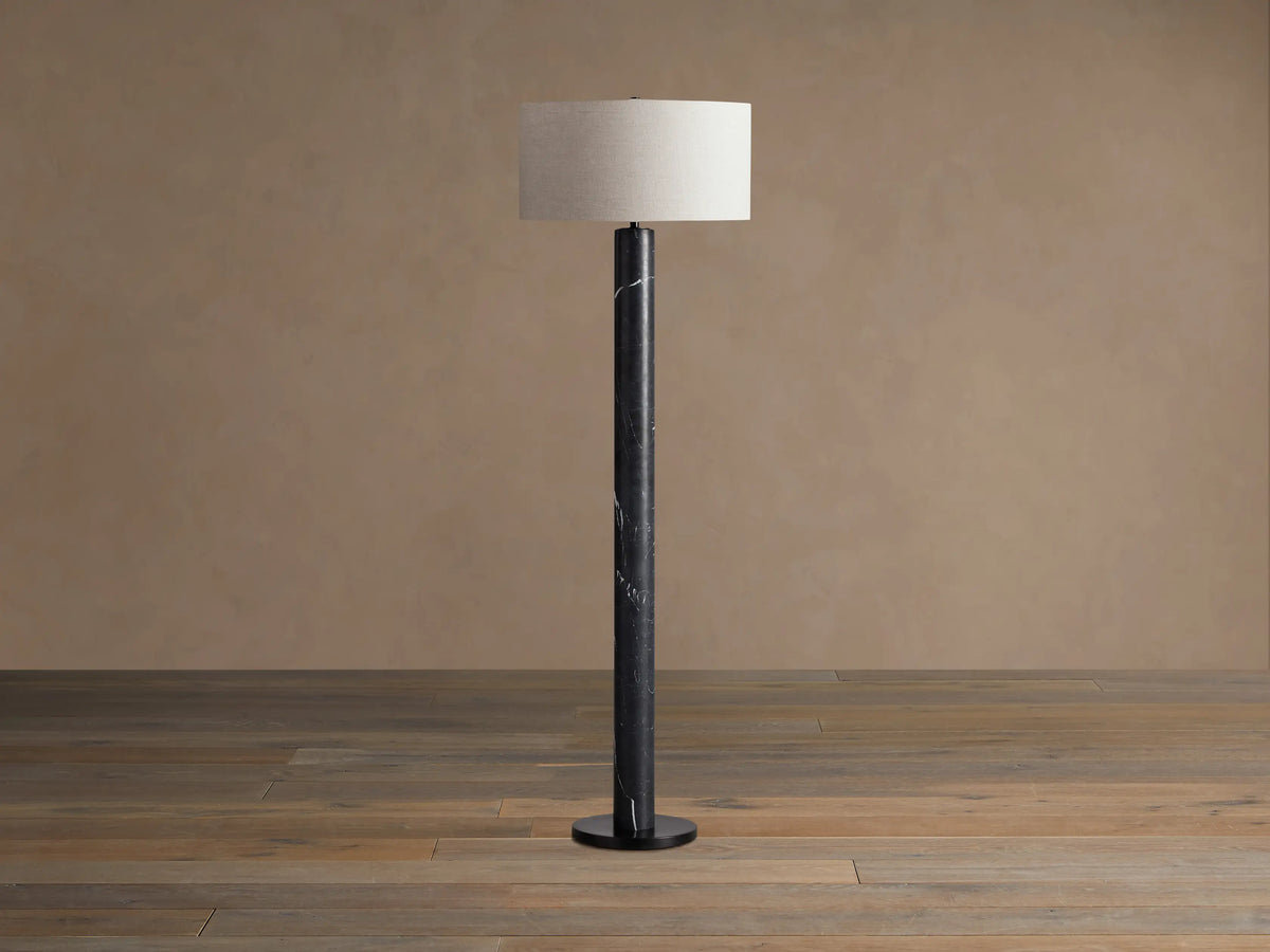 Brixton Floor Lamp with a tall, cylindrical black marble base featuring white veining and a light beige fabric drum shade.