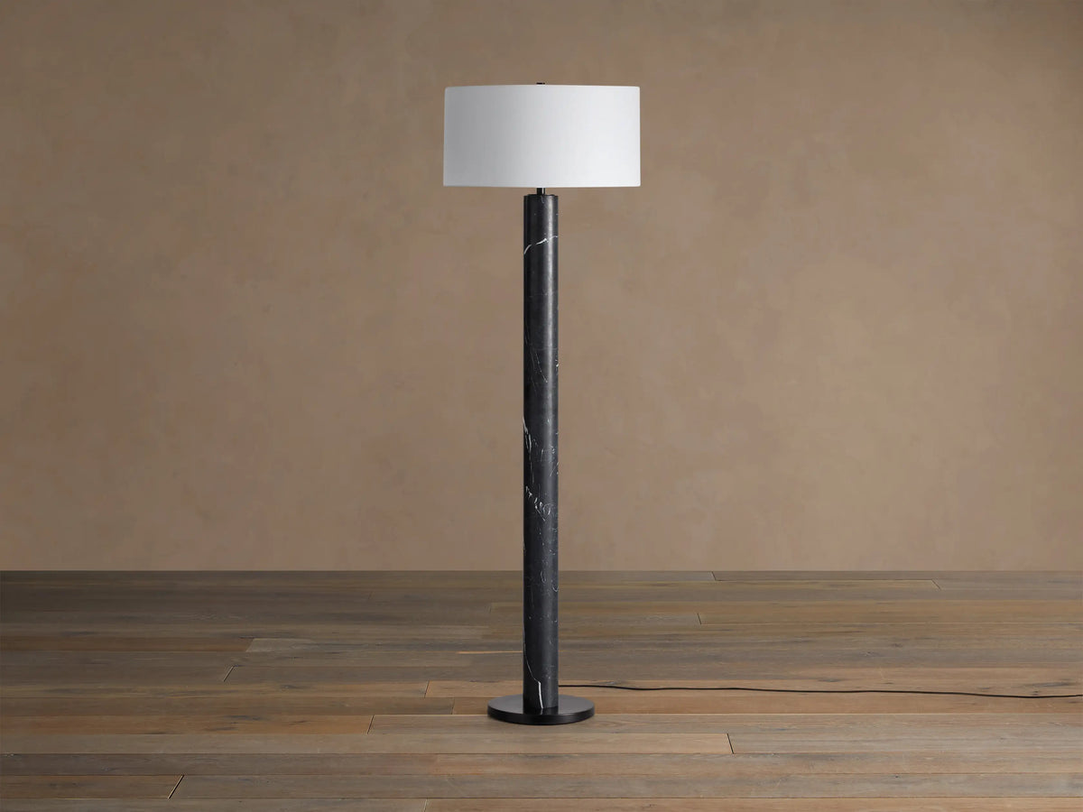 Brixton Floor Lamp: tall black marble column with white veining, white cylindrical shade, round black base, on wood floor.