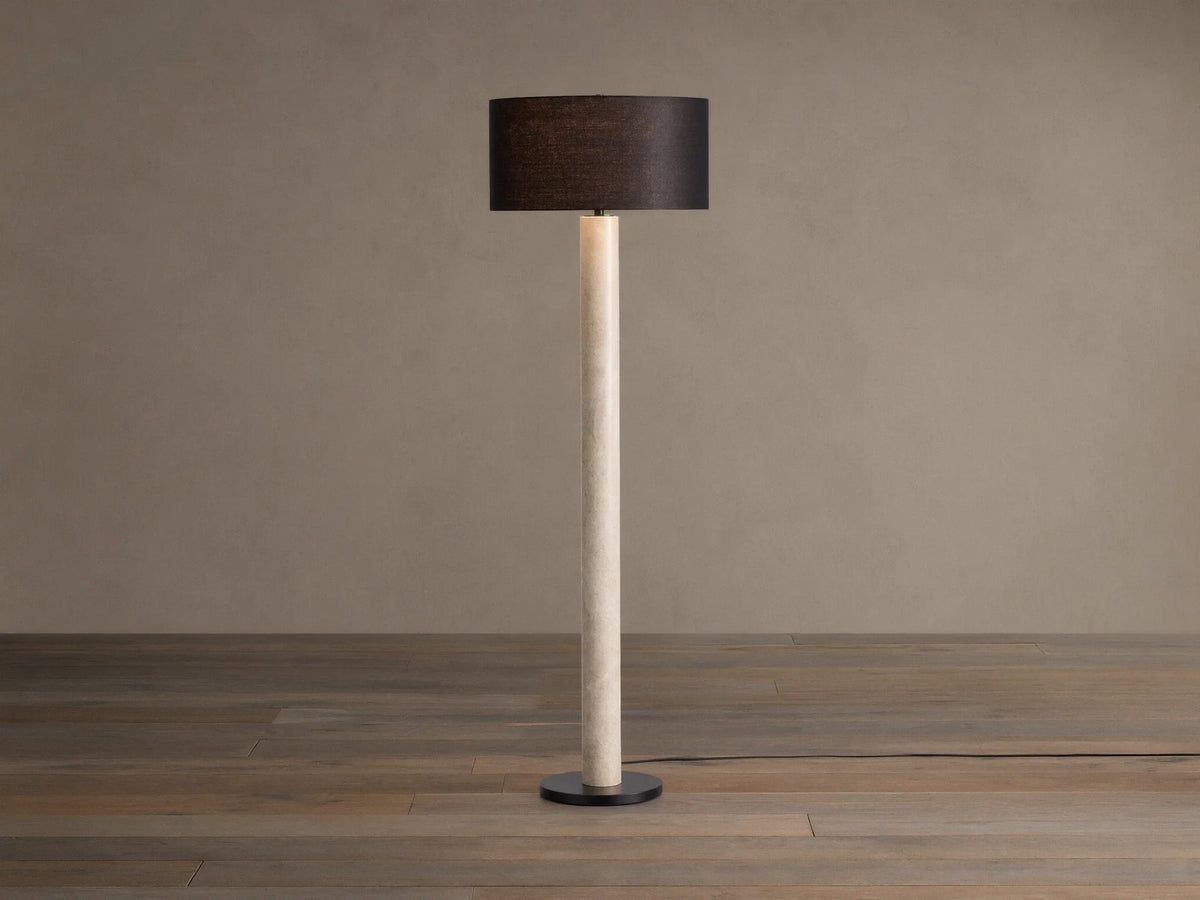 Brixton Floor Lamp with tall light marble-patterned column, dark cylindrical shade, and black round base. Against a plain wall.