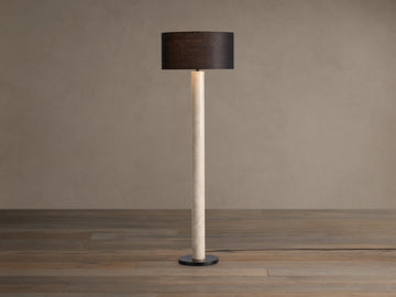 Brixton Floor Lamp with tall light marble-patterned column, dark cylindrical shade, and black round base. Against a plain wall.