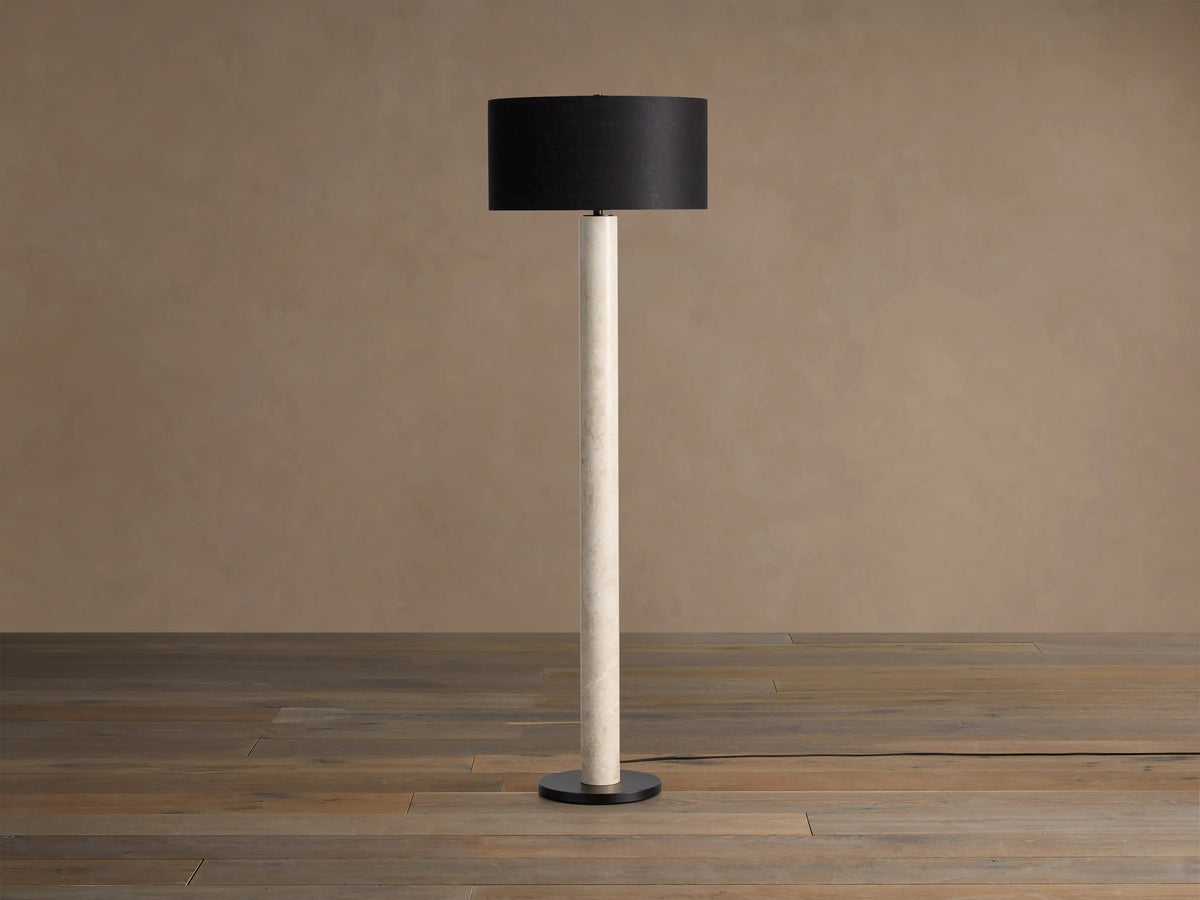 Brixton Floor Lamp with tall light marble-patterned column, dark cylindrical shade, and black round base. Against a plain wall.