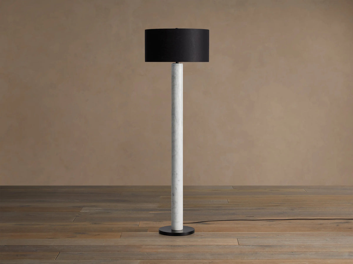 Brixton Floor Lamp with a white marble column, dark fabric drum shade, and black steel base, standing on a wooden floor.