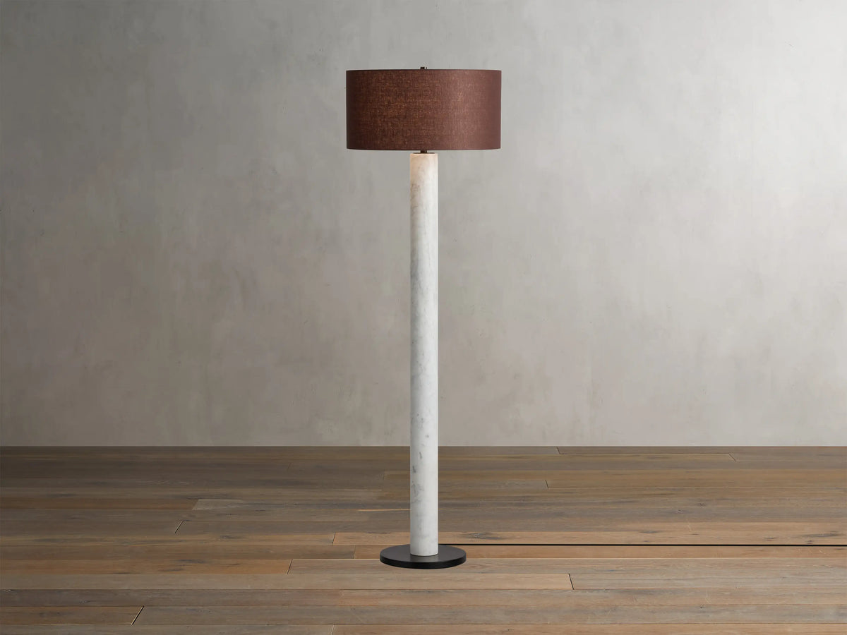 Brixton Floor Lamp with a slender white marble column, dark round base, and a brown fabric drum shade on a wooden floor.