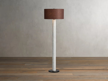 Brixton Floor Lamp with a slender white marble column, dark round base, and a brown fabric drum shade on a wooden floor.