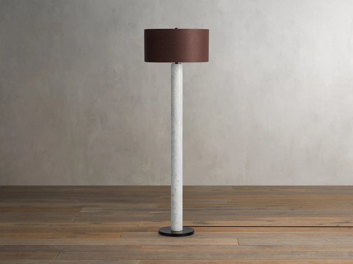 Brixton Floor Lamp with a slender white marble column, dark round base, and a brown fabric drum shade on a wooden floor.