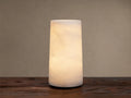 Kelby Outdoor Rechargeable Lamp: Glowing cylindrical alabaster lamp with natural veining, sitting on a rustic wooden table.