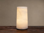 Kelby Outdoor Rechargeable Lamp: Glowing cylindrical alabaster lamp with natural veining, sitting on a rustic wooden table.