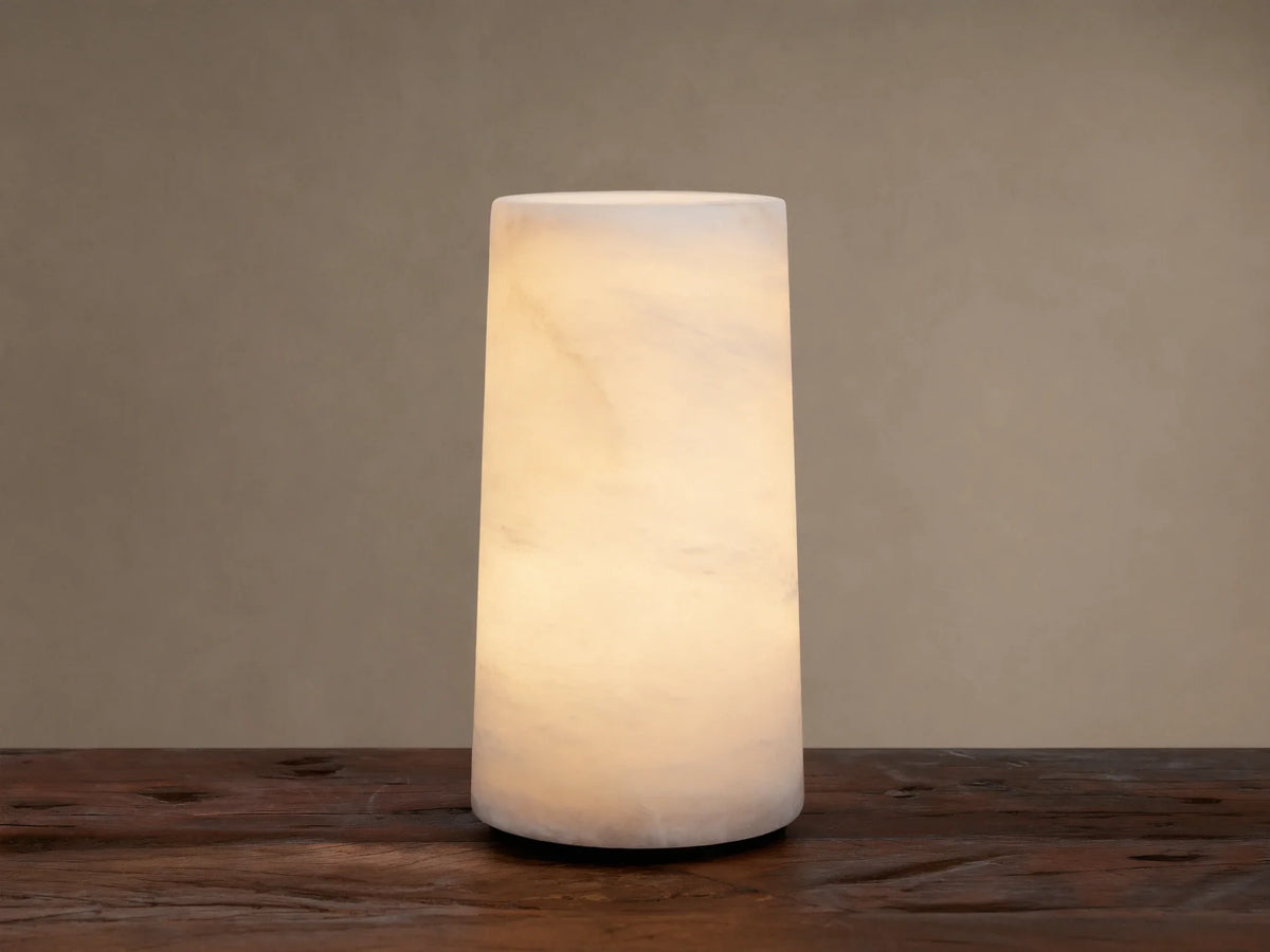 Kelby Outdoor Rechargeable Lamp: Glowing cylindrical alabaster lamp with natural veining, sitting on a rustic wooden table.