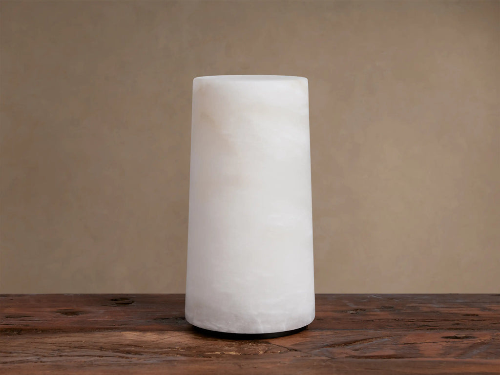 Kelby Outdoor Rechargeable Lamp: Glowing cylindrical alabaster lamp with natural veining, sitting on a rustic wooden table.
