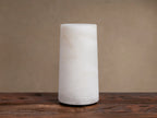 Kelby Outdoor Rechargeable Lamp: Glowing cylindrical alabaster lamp with natural veining, sitting on a rustic wooden table.